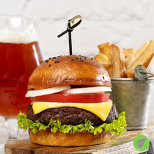 Load image into Gallery viewer, Hamburger with cheese, lettuce, and tomato on a wooden board with fries and a drink in the background, with a knot pick skewer holding the burger together
